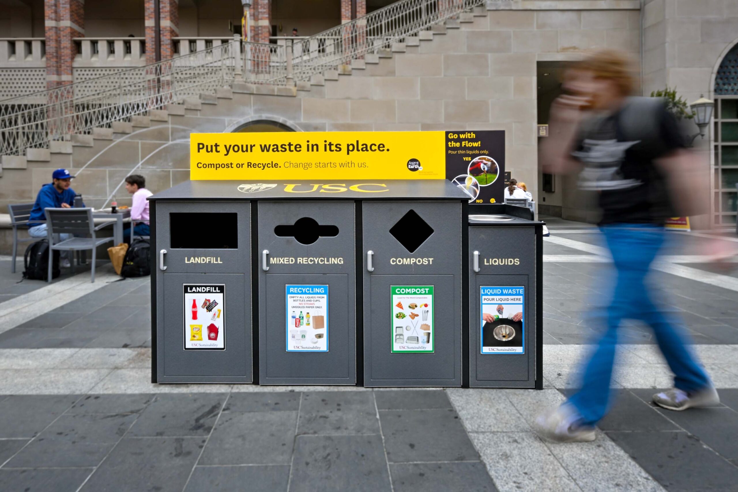 student walking by recycle bins